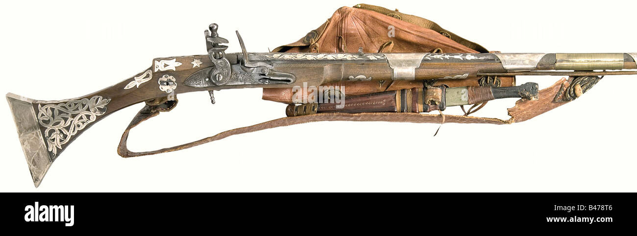A flintlock musket, Algeria, dated 1842. Long barrel with smooth bore in 14 mm calibre with fixed sights. The rear third of the barrel is decorated with raised silver flowery vines. The tang is dated '1258' (= 1842). European flintlock with floral engraving (mechanism defective). The wooden full stock is lavishly decorated with (stamped) silver and has eight silver barrel bands with floral engraving. Wooden ramrod. Leather sling and lock cover attached. Length 170 cm. There is also a Tuareg arm dagger with a double-edged blade and (damaged) wooden grip. Decorat, Stock Photo