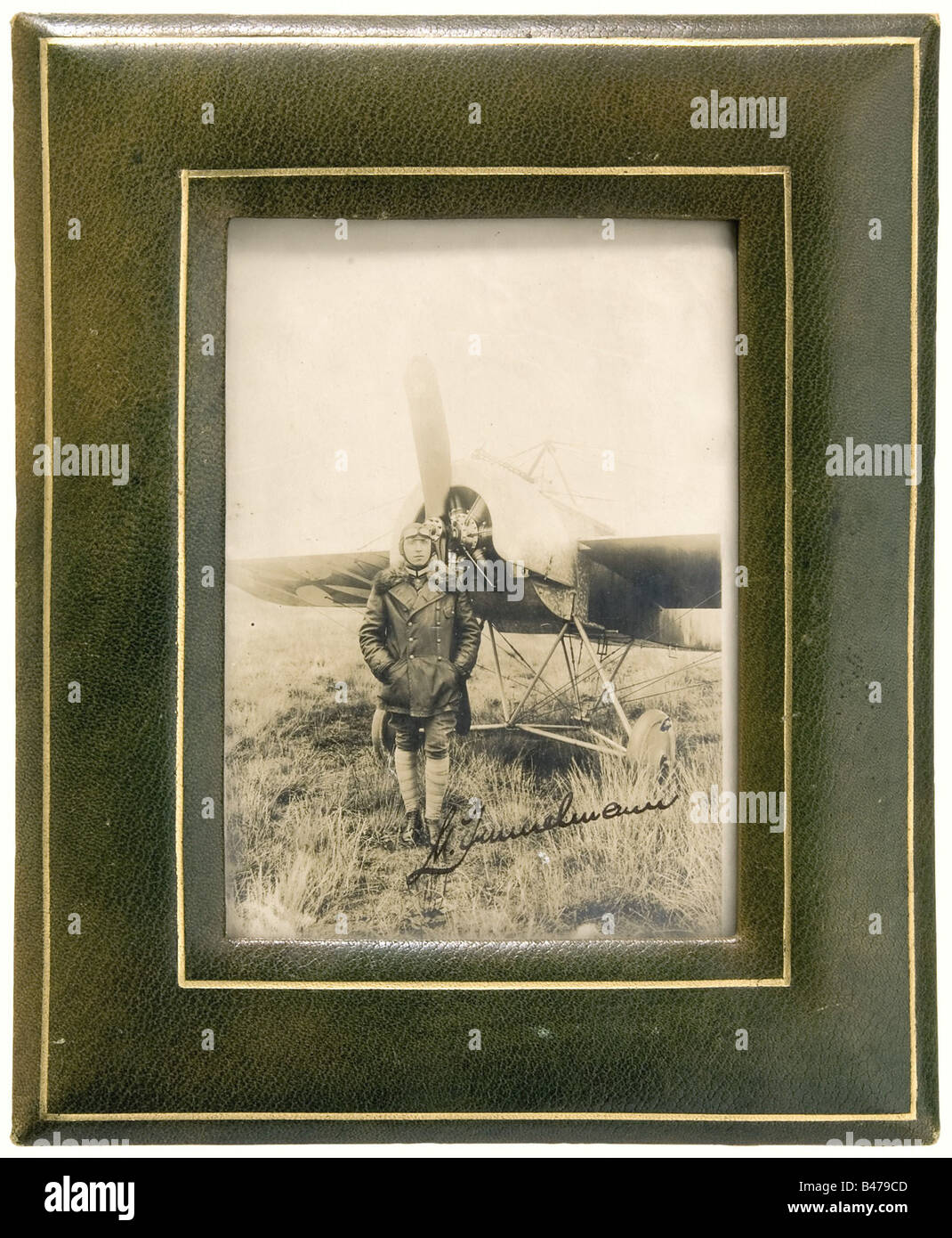 Max Immelmann - a portrait photograph with autograph 'M. Immelmann'., Immelmann wearing a leather flight jacket with fur collar, flying cap, goggles and puttees, standing with his hands in his pockets in front of his Fokker Monoplane E I 3/15. In the lower part of the picture his autograph 'M. Immelmann' in black-blue ink. In a gold embossed frame (with stand) made of green leather. Overall size 27 x 22 cm. The picture was taken shortly after Immelmann s first air victory on August 1st, 1915, after he had brought down the British Lieutenant William Reid in his , Stock Photo
