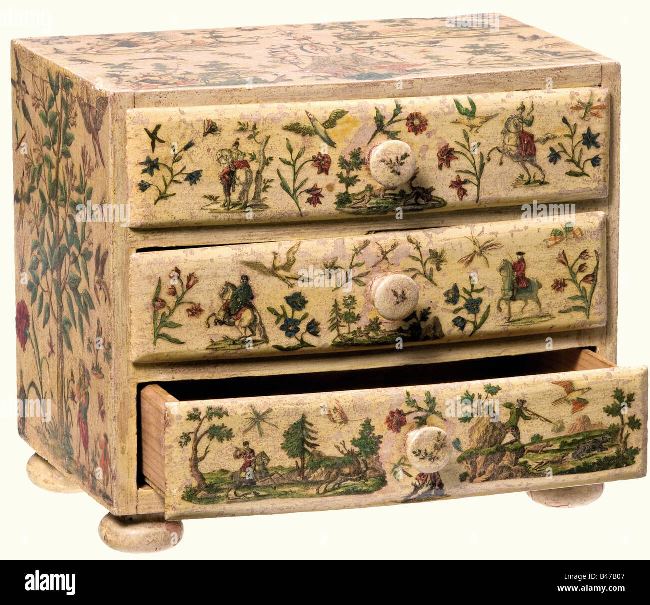 A miniature commode decorated with hunting themes, Southern German, circa 1760 A three drawer, slightly curved, soft wood commode on four compressed spherical feet. The front is painted in a cream colour and bears appliqué decoration of finely cut, coloured copperplate engraving. Surrounded with numerous hunting scenes, framed by flowers, birds, and insects. Dimensions 16.5 x 19 x 13.5 cm. historic, historical, 18th century, handicrafts, handcraft, craft, object, objects, stills, clipping, clippings, cut out, cut-out, cut-outs, storage, box, boxes, cabinet, che, Stock Photo