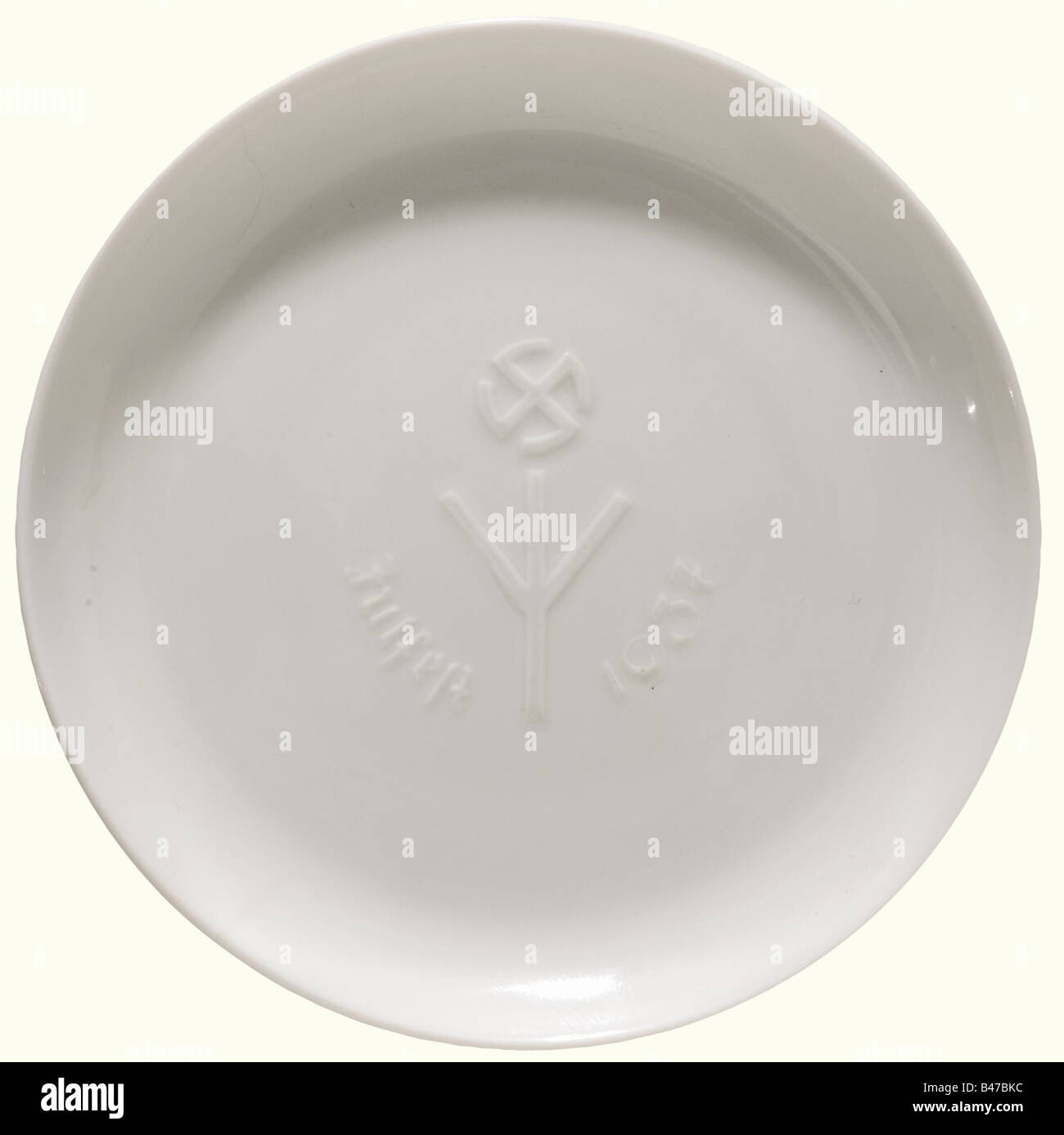 A plate commemorating the Festival of Yule 1937, Porcelain Manufacture Allach White, glazed porcelain. In the centre a reliefed life rune with sun wheel and inscription 'Julfest 1937'. On the base the green manufacturer's mark 'SS Allach'. Diameter 10 cm. The plate is depicted in Heinrich W. Schild, 'Julteller mit den Runen der Porzellan-Manufaktur Allach-München GmbH' in Militaria - Fachjournal für Auszeichnungen, Uniformierung, Militär- und Zeitgeschichte, issue 1, 2005, p. 11, illustrations 7a, b. Sample specimen, probably a unique copy. Of extremest rarity., Stock Photo