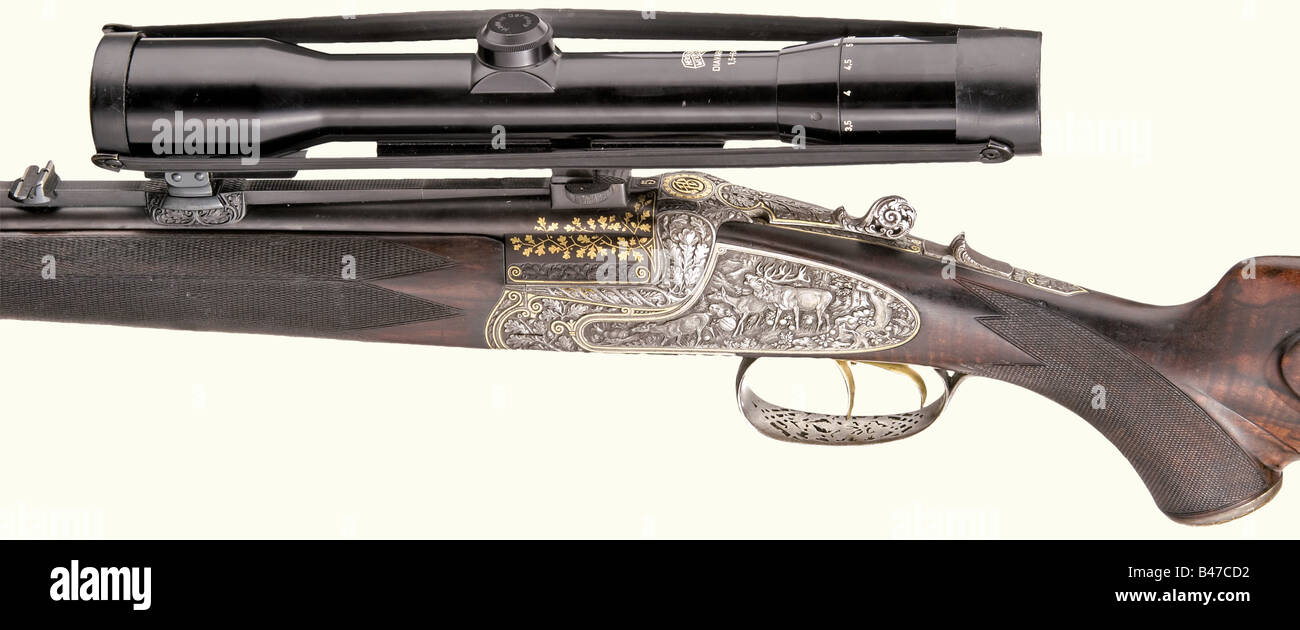 A magnificent over-and-under double-barrelled rifle, Merkel in Suhl. Calibres 5.6 x 35 R and 6.5 x 57 R, no. 24444. Blued barrels with guilloched rib. Dovetailed folding sight, at the breech oak leaf decoration in gold inlay. Locks and frame with deep, high-quality engraving showing game sceneries in half-relief. The surrounding contours in gold. On the upper side monogrammed 'AB'. Gold-plated set triggers, slide safety. Beautifully grained walnut half stock with fine checkering. Richly chiselled iron furniture with gold inlay. Openworked trigger guard, pommel , Stock Photo
