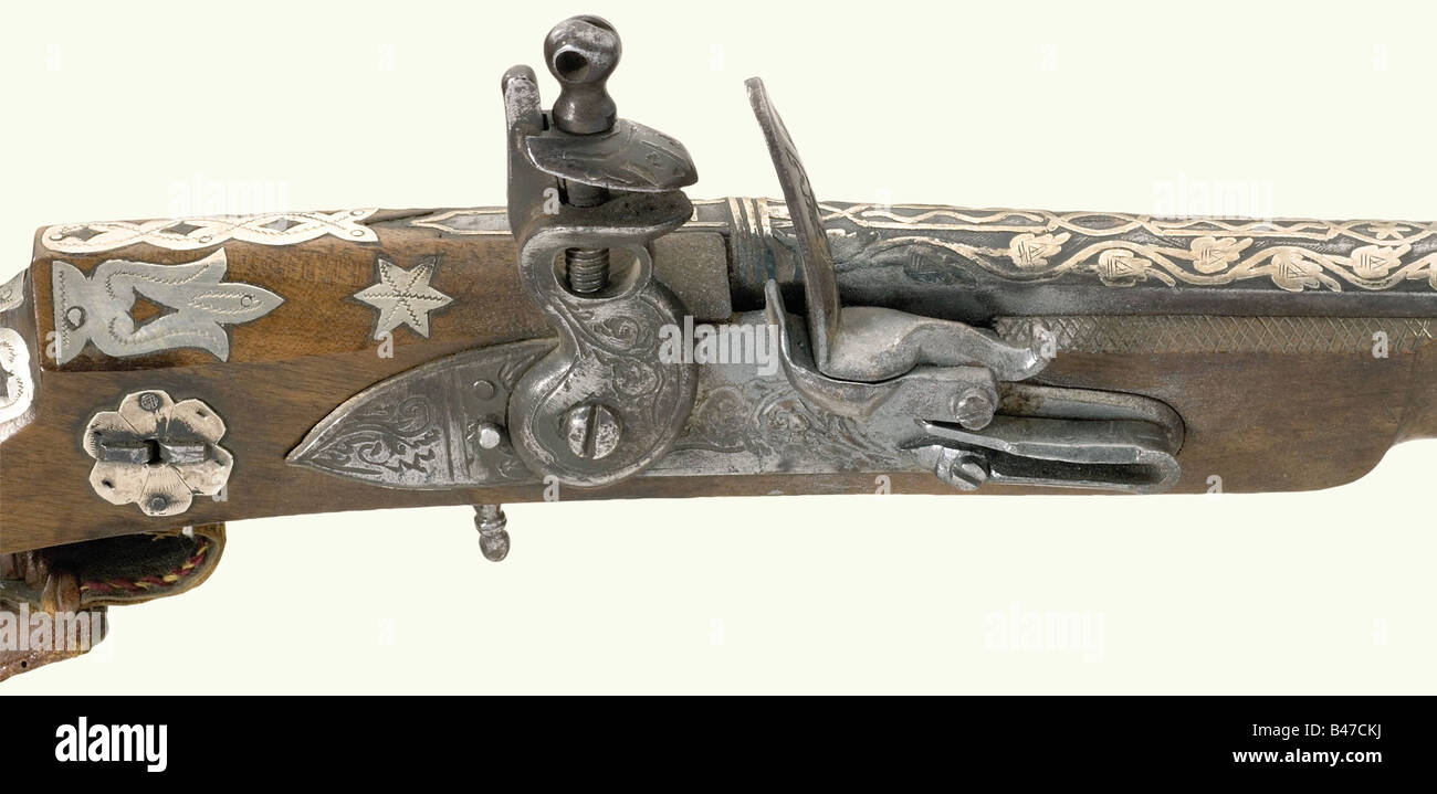 A flintlock musket, Algeria, dated 1842. Long barrel with smooth bore in 14 mm calibre with fixed sights. The rear third of the barrel is decorated with raised silver flowery vines. The tang is dated '1258' (= 1842). European flintlock with floral engraving (mechanism defective). The wooden full stock is lavishly decorated with (stamped) silver and has eight silver barrel bands with floral engraving. Wooden ramrod. Leather sling and lock cover attached. Length 170 cm. There is also a Tuareg arm dagger with a double-edged blade and (damaged) wooden grip. Decorat, Stock Photo
