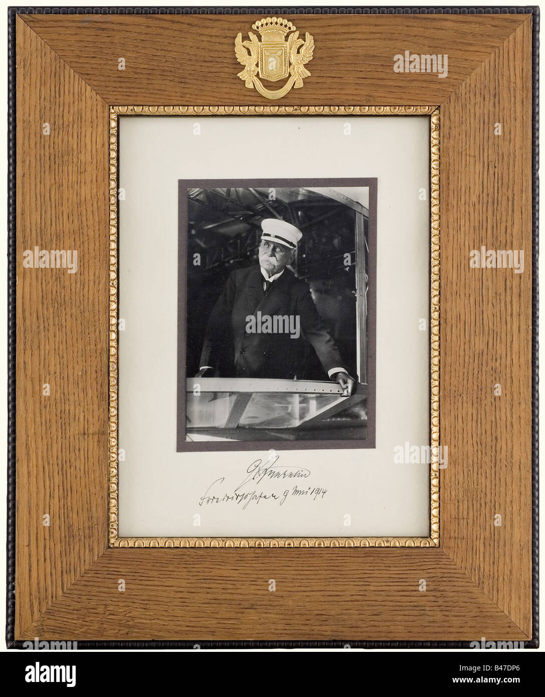 A portrait photograph of Count Ferdinand von Zeppelin., Large presentation portrait of the count on the bridge of an airship. Mount with handwritten autograph in blue ink 'Gr. Zeppelin - Friedrichshafen 9 Mai 1914'. Oak frame (47 x 56 cm) with applied gilt silver coat of arms of Count Zeppelin. On the verso an affixed envelope from the 1930s addressed to a Bavarian prince, enclosed old picture postcards ZI, an admission ticket for the airship viewing and an original letter paper of the German Zeppelin shipping company 'Luftschiff Hindenburg - An Bord' with a pi, Stock Photo