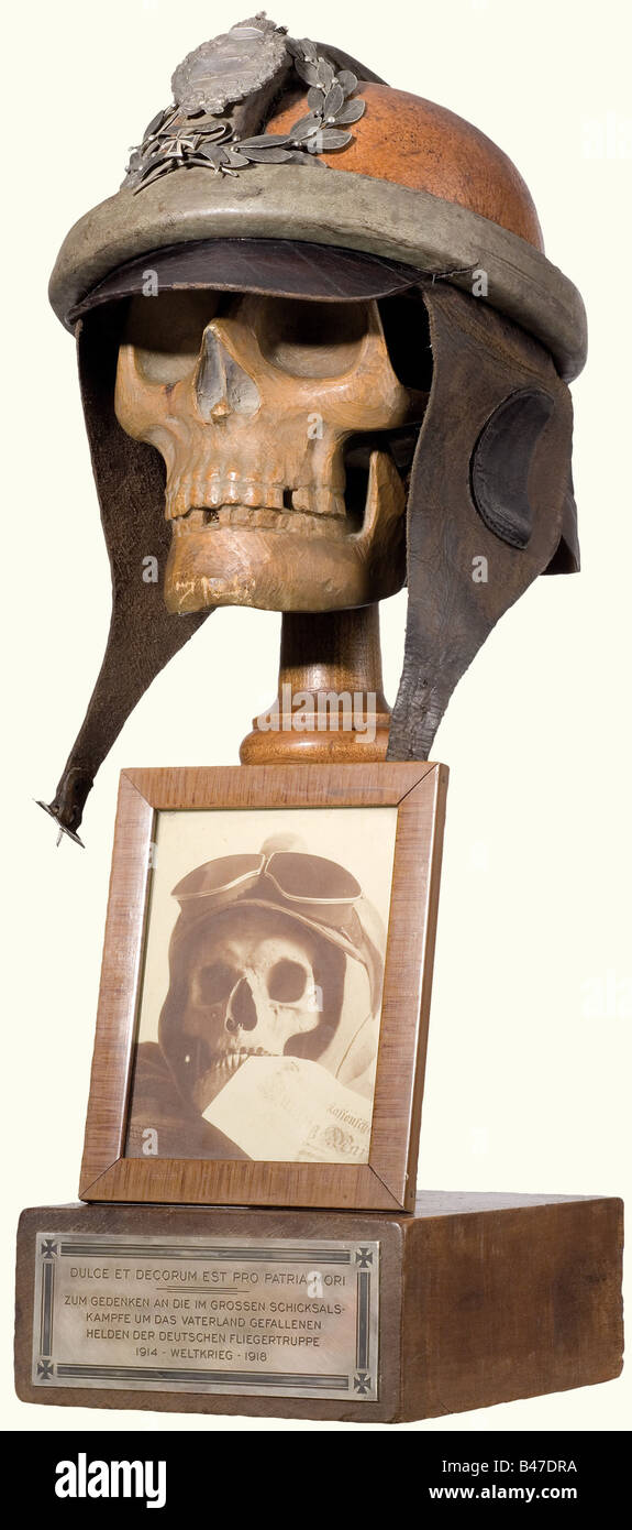 A memento mori for the German Airmen, of the First World War. A skull carved from fruitwood with a leather pilot's helmet, the nape of the helmet inscribed 'Flg.Bekl. Döberitz 1918', and the visor is stamped 'Hans Amler Original'. The Military Pilot's Insignia (20th Year) is laid on top of the helmet in a laurel wreath with a miniature Iron Cross 1914 beneath a scroll, '1914 Weltkrieg 1918' (1914 World War 1918). A framed contemporary photograph of a genuine skull with flyer's helmet and goggles with a fifty mark bill between his teeth is mounted on the front o, Stock Photo