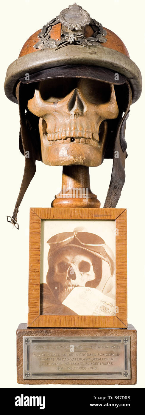 A memento mori for the German Airmen, of the First World War. A skull carved from fruitwood with a leather pilot's helmet, the nape of the helmet inscribed 'Flg.Bekl. Döberitz 1918', and the visor is stamped 'Hans Amler Original'. The Military Pilot's Insignia (20th Year) is laid on top of the helmet in a laurel wreath with a miniature Iron Cross 1914 beneath a scroll, '1914 Weltkrieg 1918' (1914 World War 1918). A framed contemporary photograph of a genuine skull with flyer's helmet and goggles with a fifty mark bill between his teeth is mounted on the front o, Stock Photo