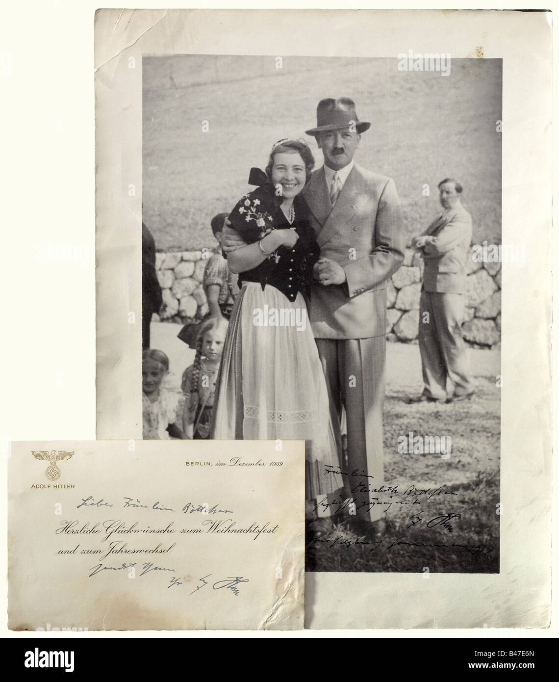 Adolf Hitler., A handwritten dedication and autograph in ink (transl.) 'Cordially dedicated to Miss Elisabeth Böttcher, Adolf Hitler - Obersalzberg, Sommer 1937' on large-size photo (ca. 30 x 40 cm), Hitler in civilian clothes linking arms with Miss Böttcher, on the verso stamped 'Aufn. Photo J. Schmid, Berchtesgaden'. Additionally a Christmas/New Year Greeting Card from 1939 with raised golden eagle over 'Adolf Hitler', pre-printed congratulatory text and handwritten addition in ink (transl.) 'Dear Miss Böttcher ... Yours, Adolf Hitler', stained, in envelope. , Stock Photo