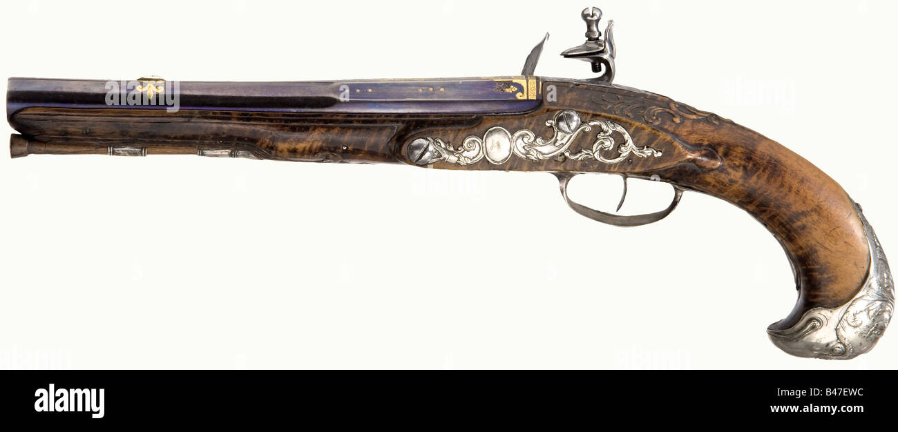 A pair of silver-mounted flintlock pistols, Pierre Peyret à Paris, circa 1740. Two-stage barrels (reblued), decorated with gold-inlaid and chased rocaille and trophies. The mark 'CN' with a crown is stamped on the side. The locks are engraved with decorative vines and rocaille with remnants of gold background. The lock plates are signed, 'Pierre Peyret à Paris' Walnut root full stocks (one forearm has an old repaired crack). With richly profiled silver furniture (chased). The pommels are worked as eagle heads. Wooden ramrods with flat iron tips. Length of each , Stock Photo