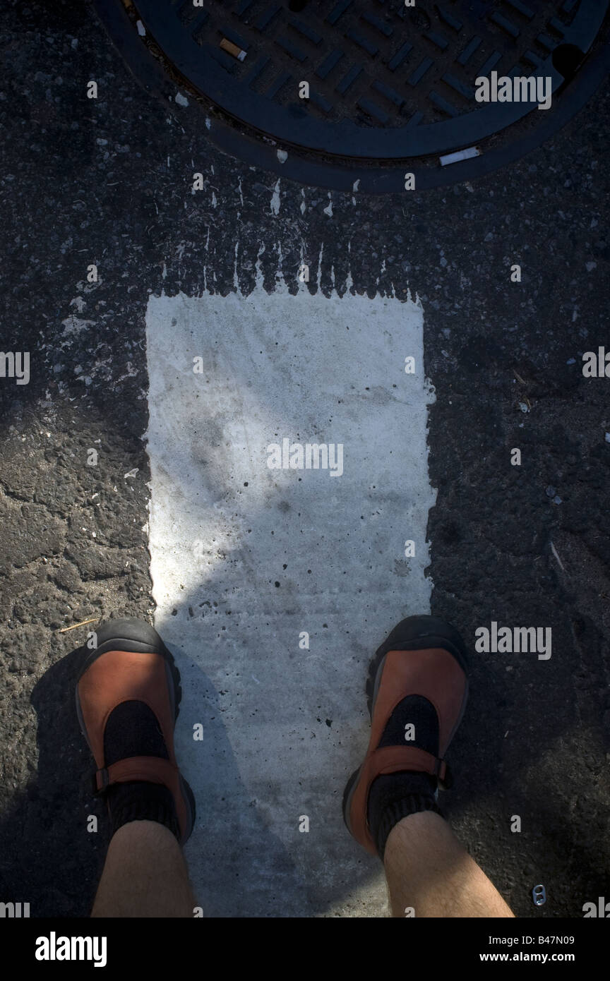 A white lane marking on an asphalt street with a pair of feet clad in red shoes Stock Photo