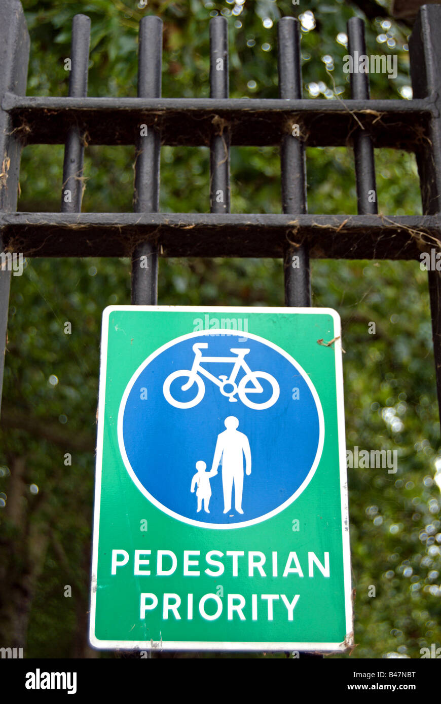 green and blue sign indicating pedestrian priority over cyclists on railings in wandsworth park, southwest london, england Stock Photo