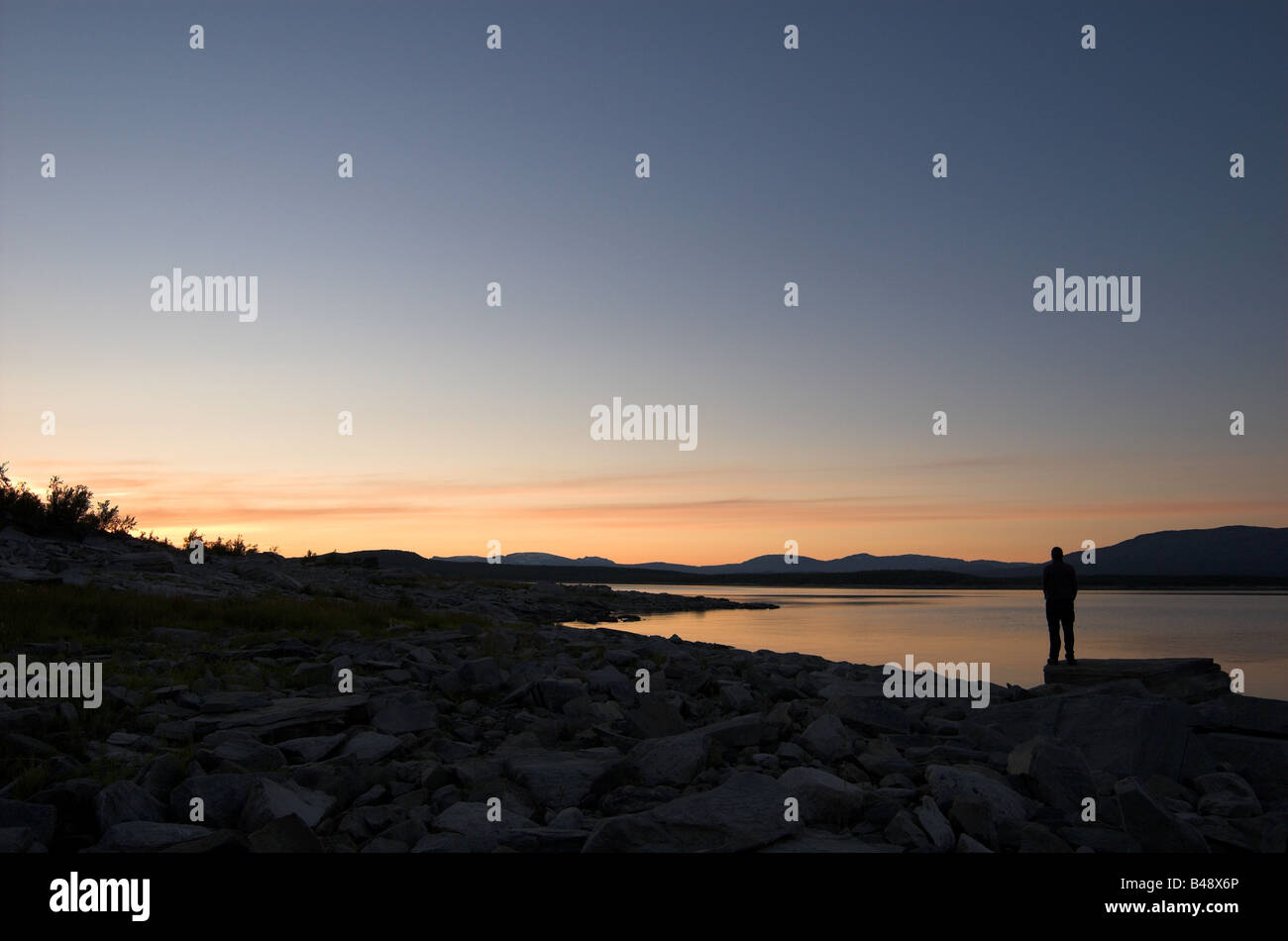 Silhouetted figure looking out over lake at sunset, Lapland / Arctic Sweden Stock Photo