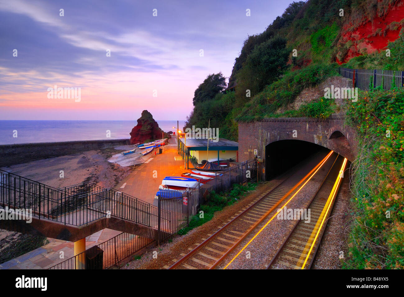 Sunrise from the railway footbridge at Dawlish in South Devon with the light trails of a train coming out of the tunnel Stock Photo