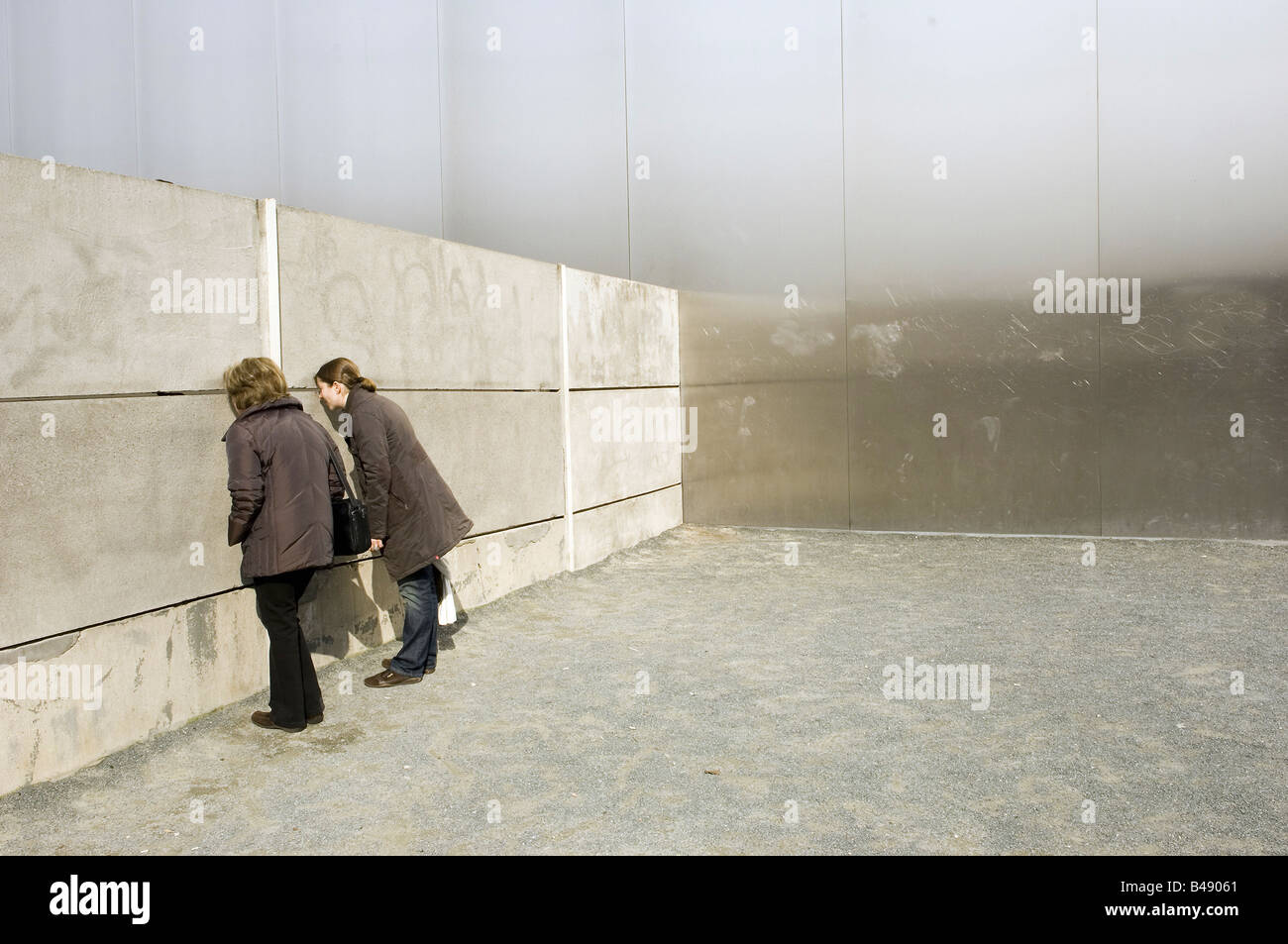 Two women looking through a slit in the remains of the Berlin Wall, Germany Stock Photo