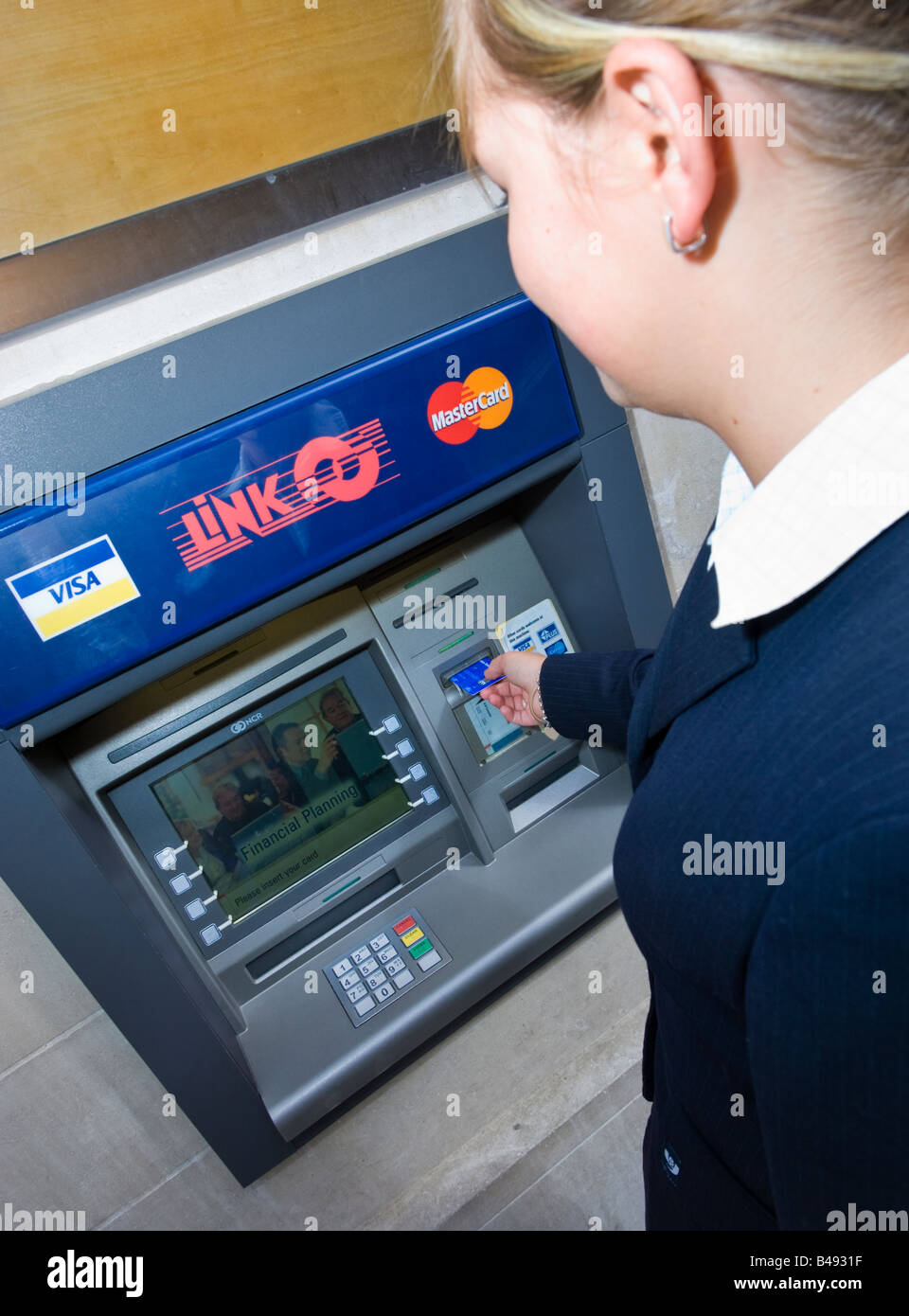 Young businesswoman in suit inserting card into a Link cash point machine ATM UK Stock Photo