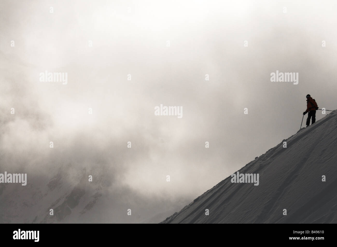 A silhouetted telemark skier on top of a slop looking over his shoulder