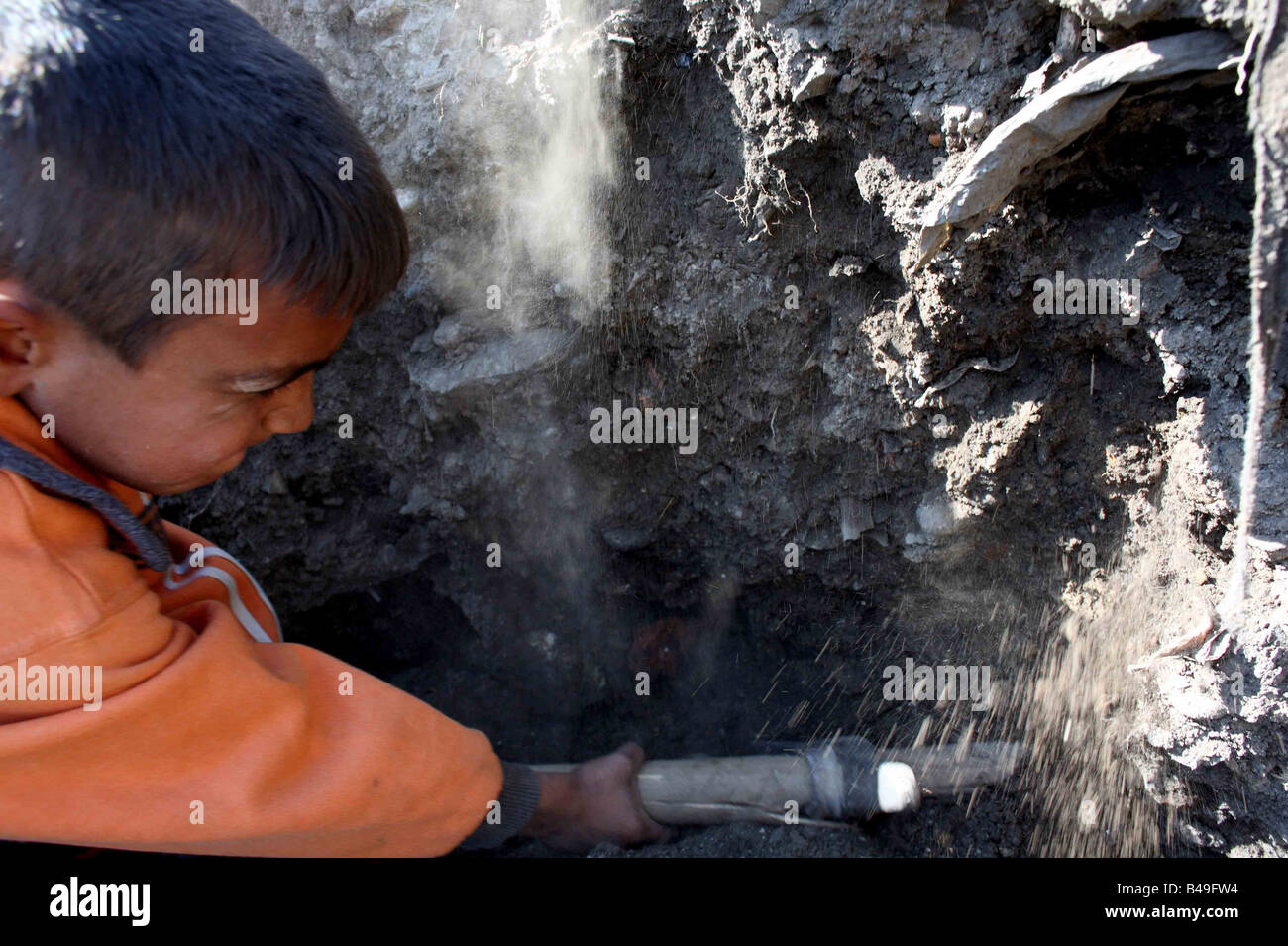 Roma gypsy child labourer working hard to dig out cans from a rubbish dump with a pick axe Stock Photo