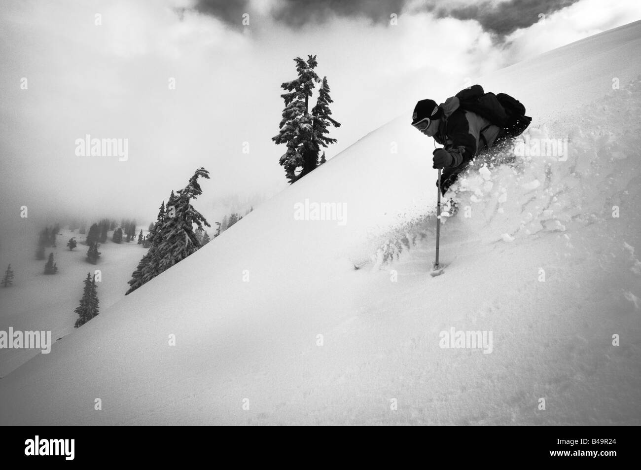 A skier descending a pristine slope and silhouetted against a cloudy sky Stock Photo