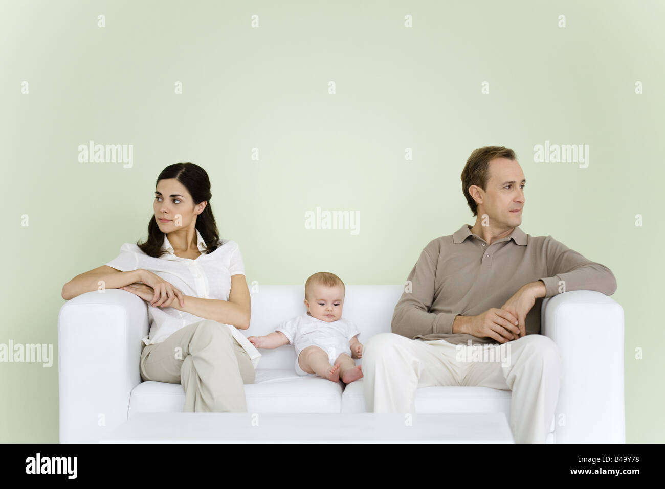 Couple sitting on couch with baby between them, both looking away Stock Photo