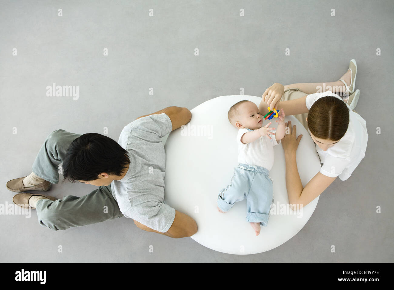 Mother playing with infant lying on ottoman, father sitting with back turned to them, overhead view Stock Photo