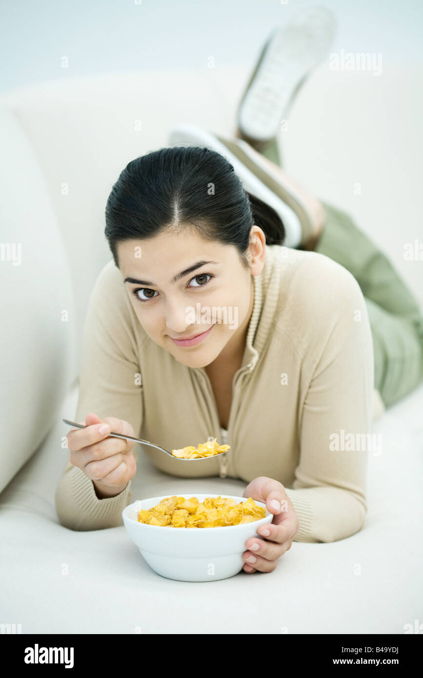 Young woman lying on stomach, eating bowl of cereal Stock Photo Alamy