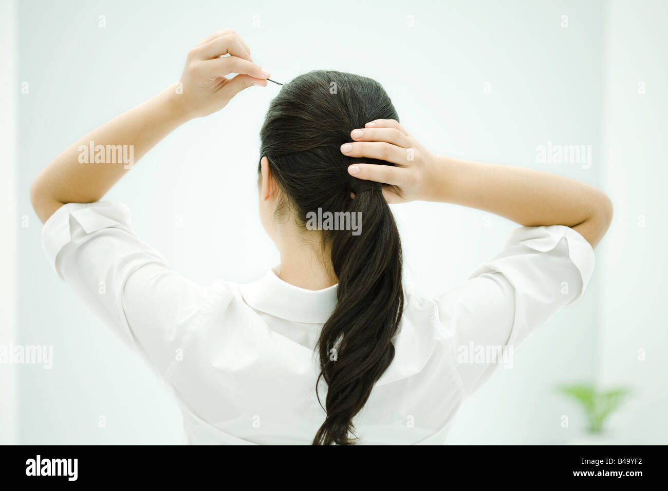 Woman putting hair in ponytail, arms raised, rear view Stock Photo