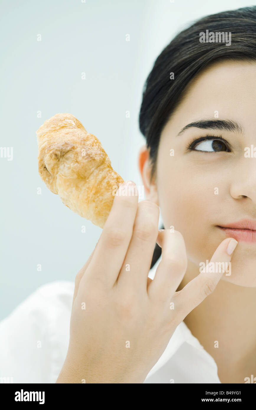Woman holding croissant, looking away, cropped Stock Photo