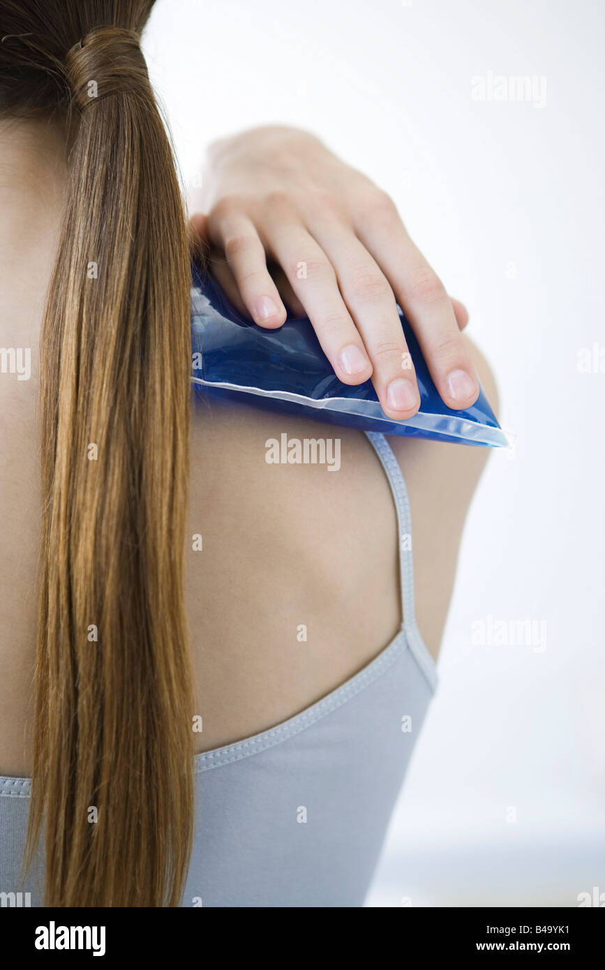 Woman holding cold compress against shoulder, cropped rear view Stock Photo