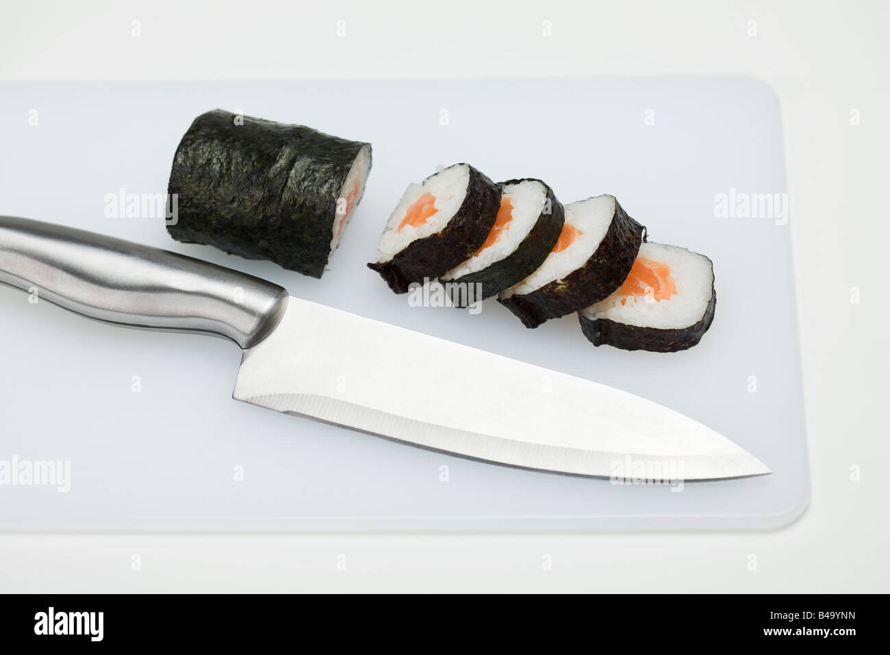 Partially sliced roll of maki sushi on cutting board with knife Stock Photo