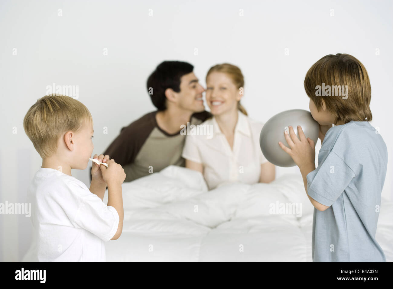 Two boys inflating balloons, parents smiling on bed in background Stock Photo
