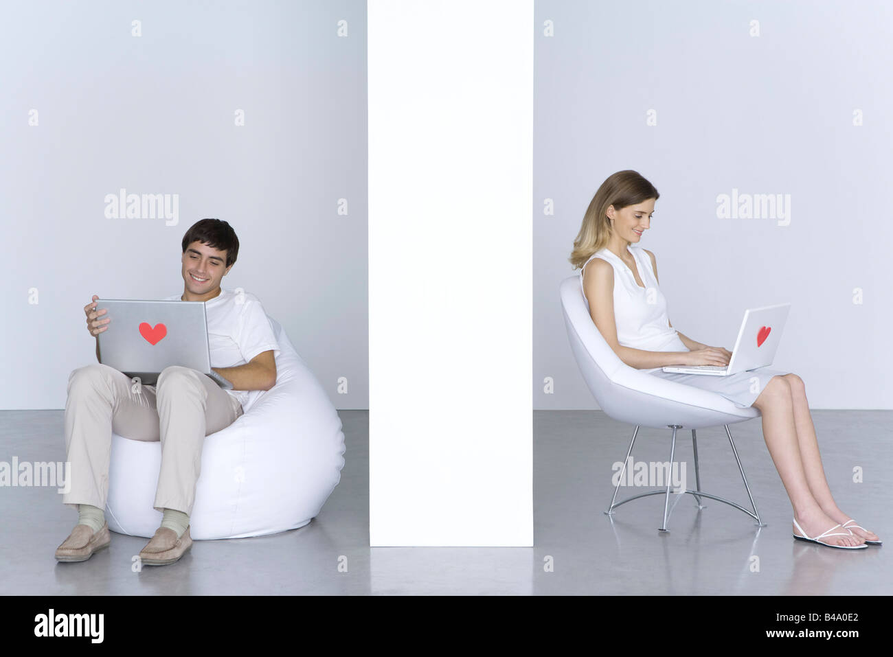 Man and woman sitting separately, using laptop computers with hearts on them, smiling Stock Photo