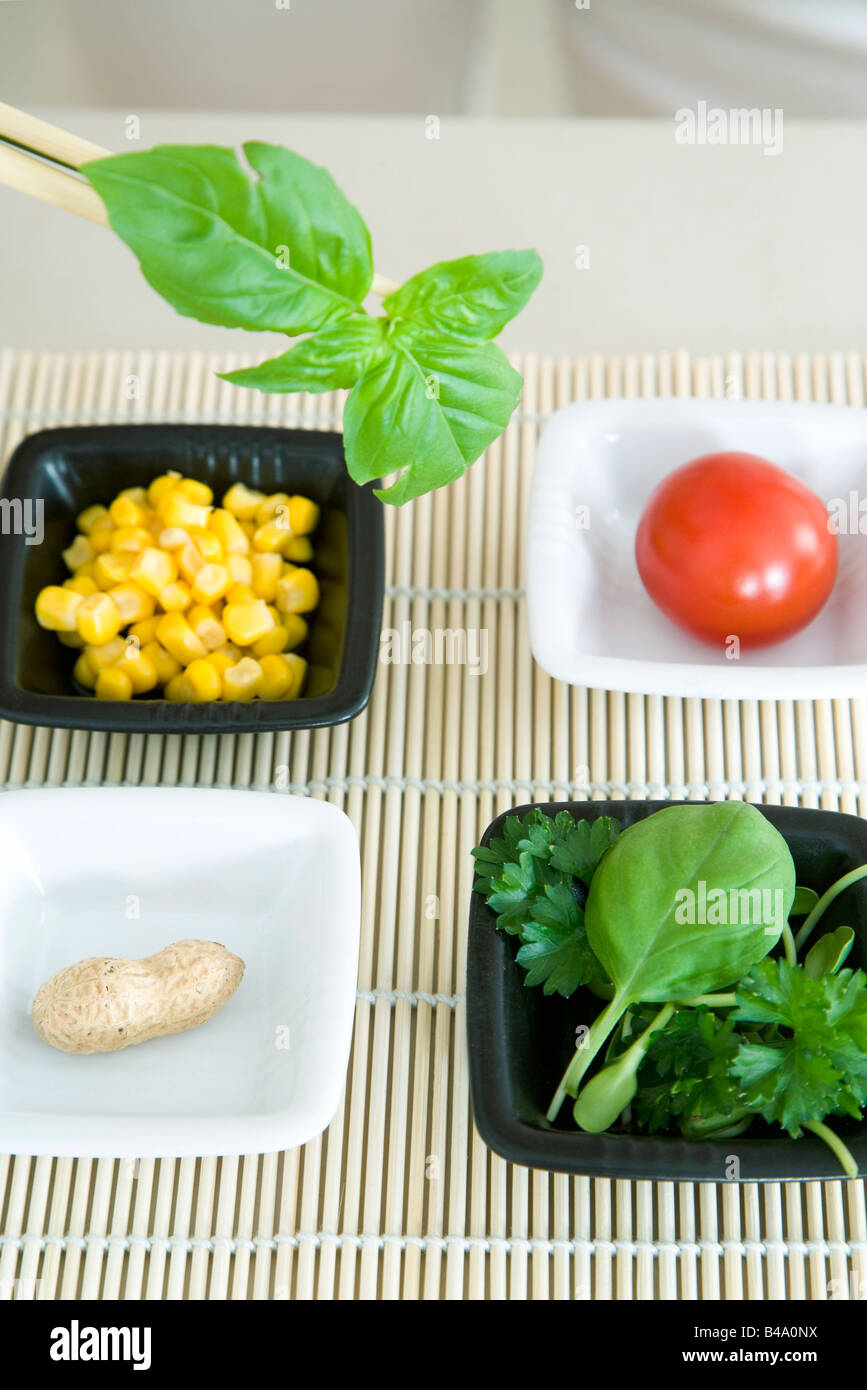 Chopsticks holding sprig of herb over several dishes of food Stock Photo