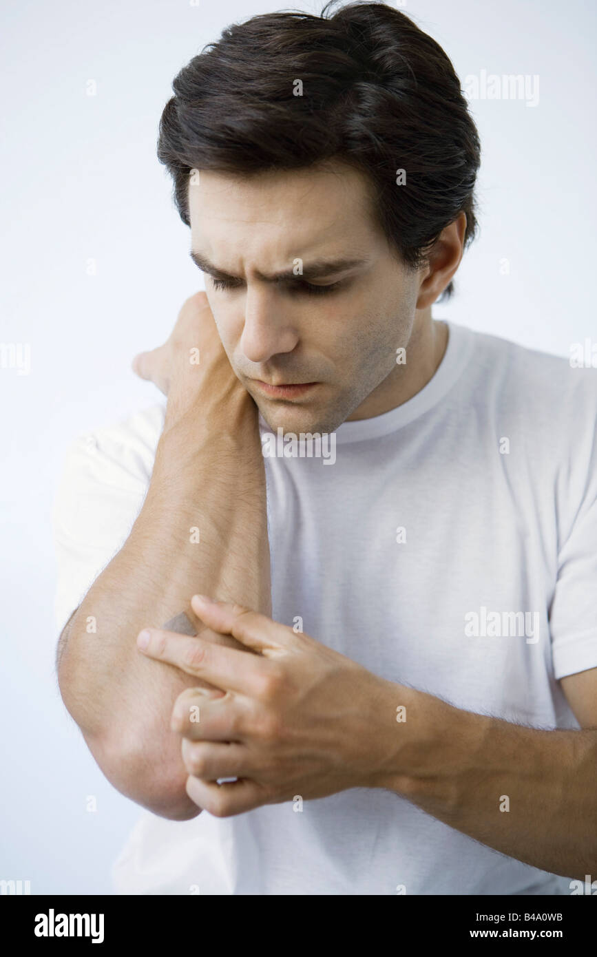 Man putting adhesive bandage on arm, frowning Stock Photo
