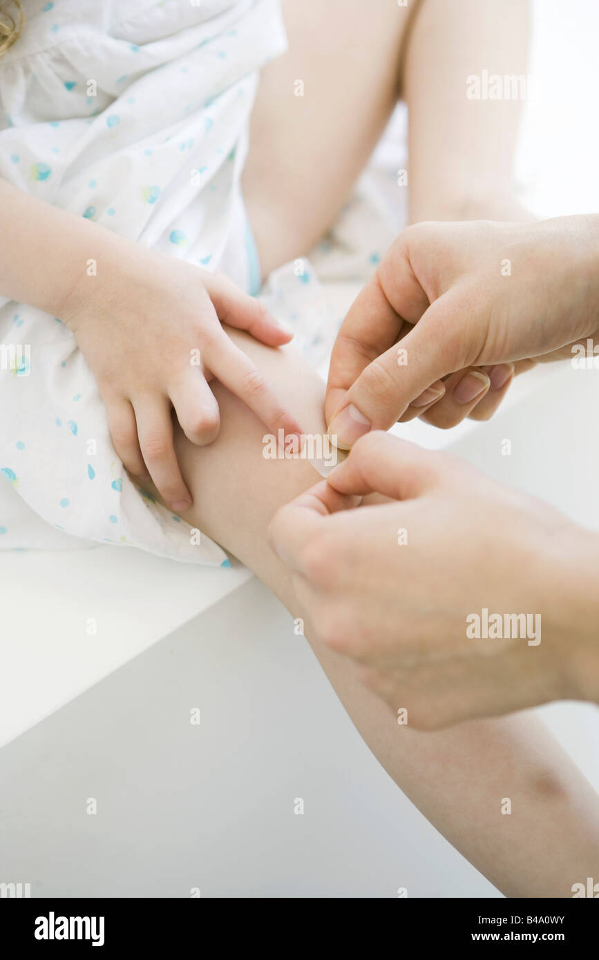 Woman putting adhesive bandage on little girl's knee, cropped view Stock Photo