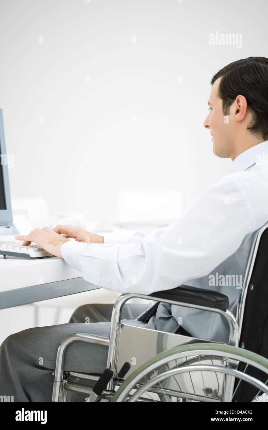 Professional man in wheelchair, typing, side view Stock Photo