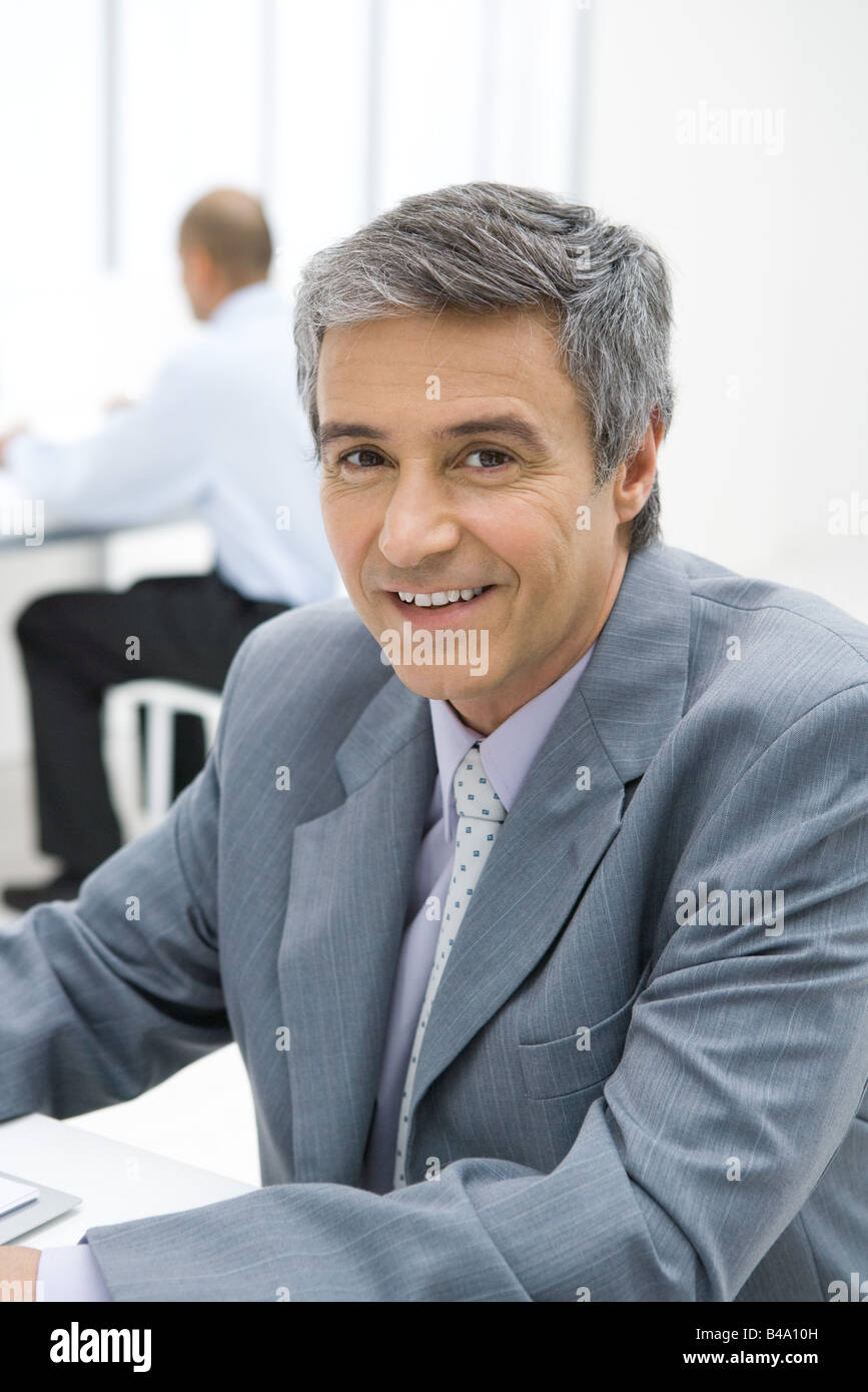 Businessman sitting in office, smiling at camera, portrait Stock Photo ...