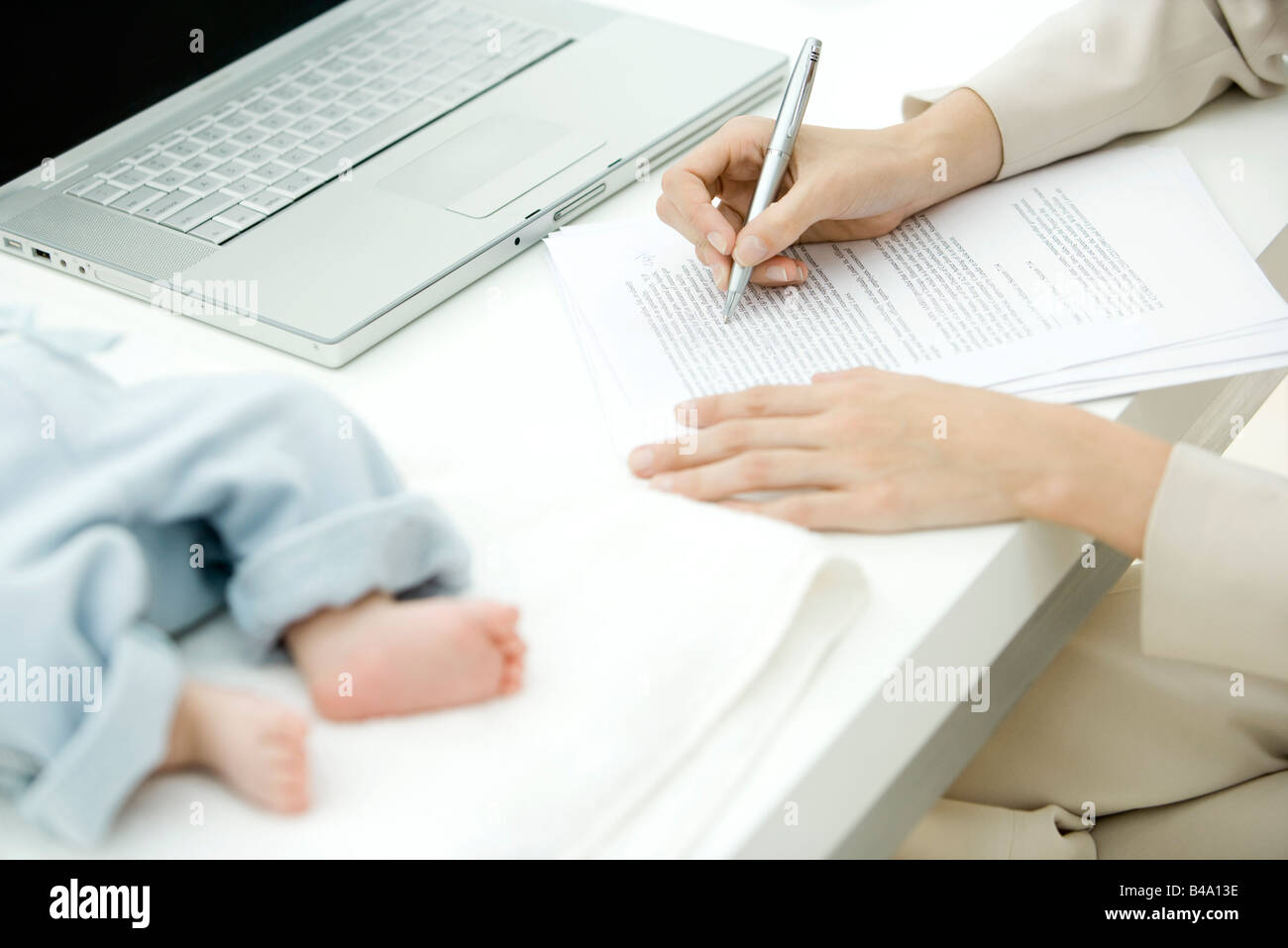 Woman editing document at desk, infant lying nearby, cropped view Stock Photo