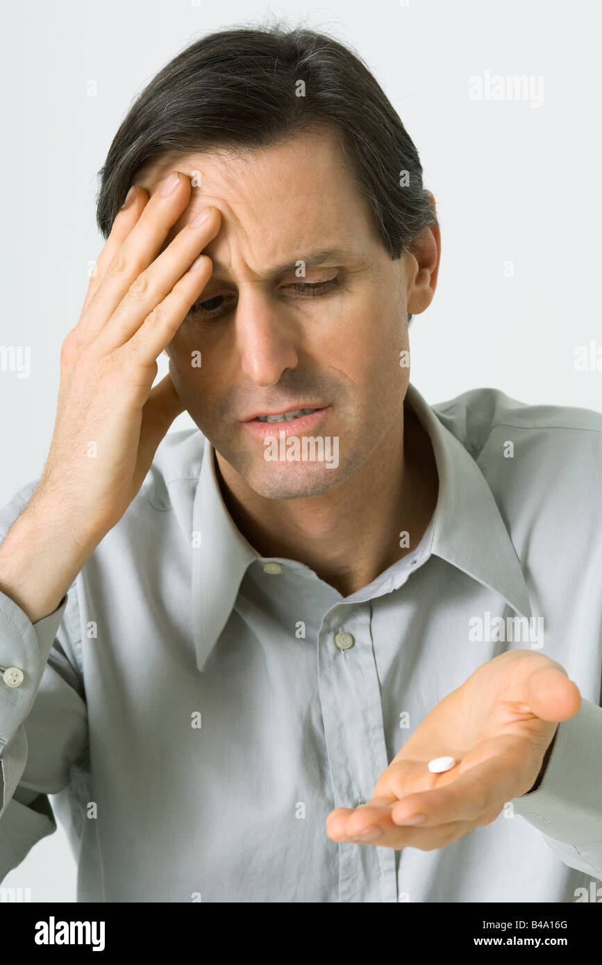 Man holding head, looking down at pill in hand Stock Photo Alamy