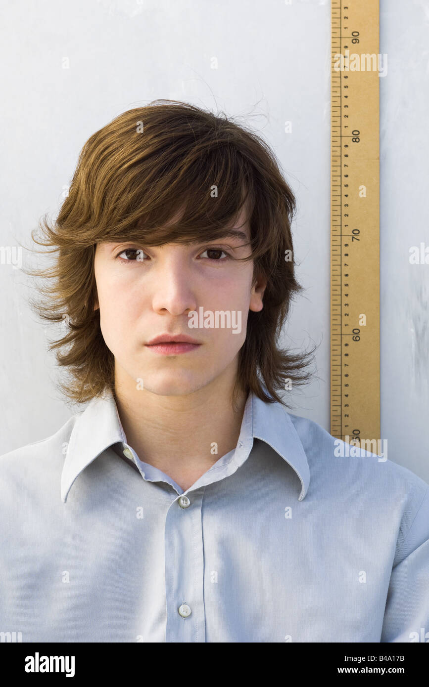 Young man standing in front of ruler, looking at camera Stock Photo