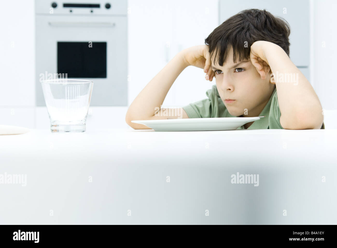 Boy sitting at dinner table, holding head, sulking Stock Photo