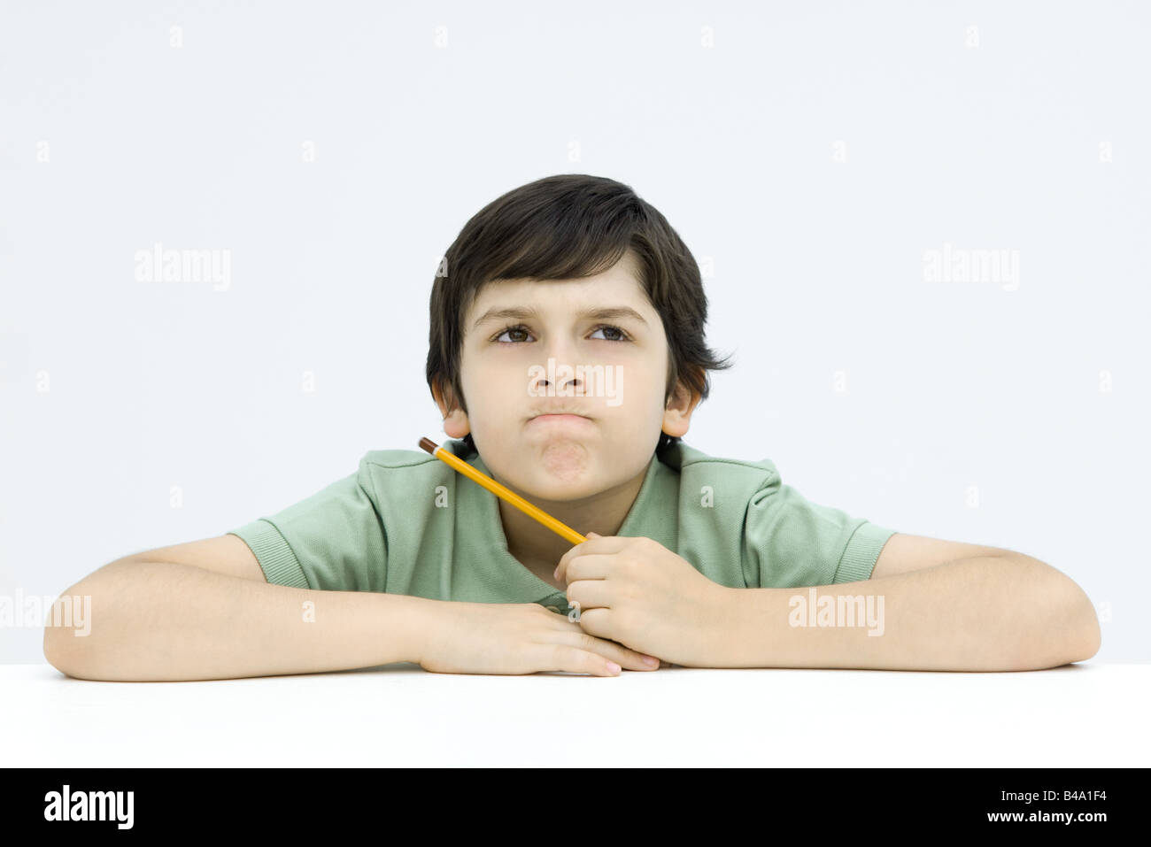 Boy holding pencil, biting lips, looking up Stock Photo