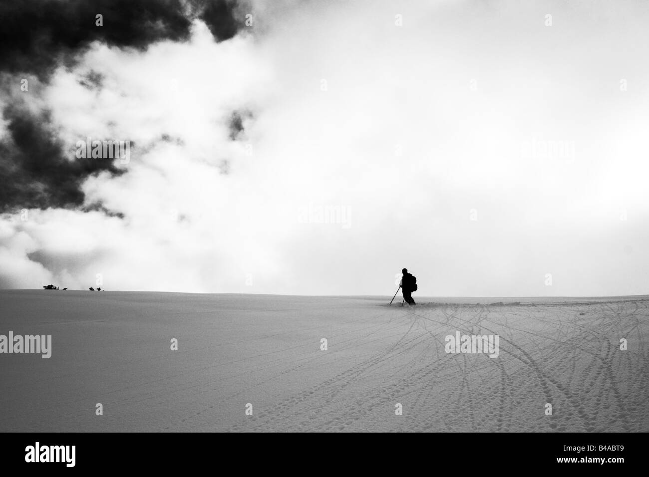 A skier standing at the top of a pristine slope and silhouetted against a cloudy sky Stock Photo