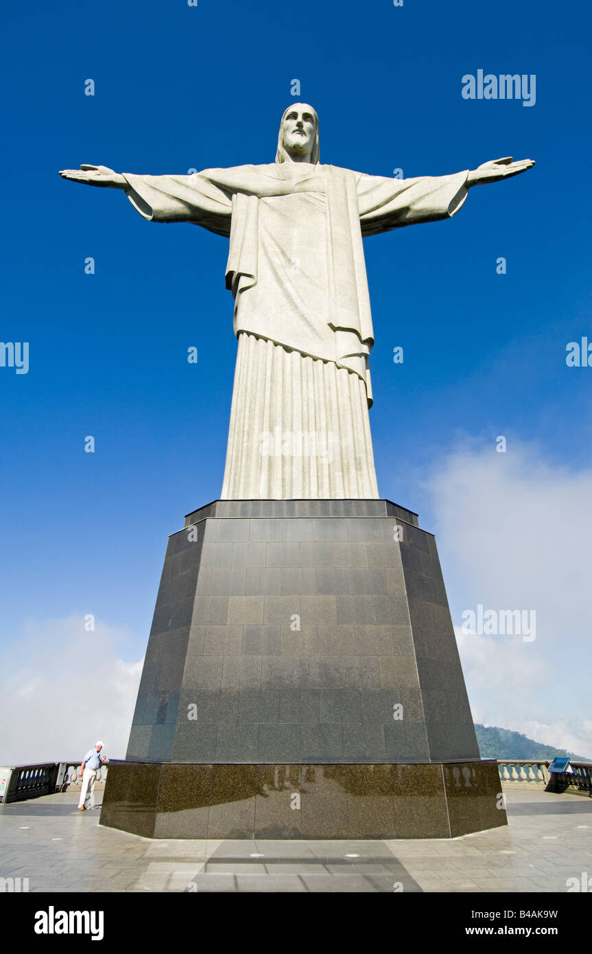 A wide angle view of the Christ the Redeemer statue overlooking Rio De Janeiro with a tourist at the base to show scale. Stock Photo