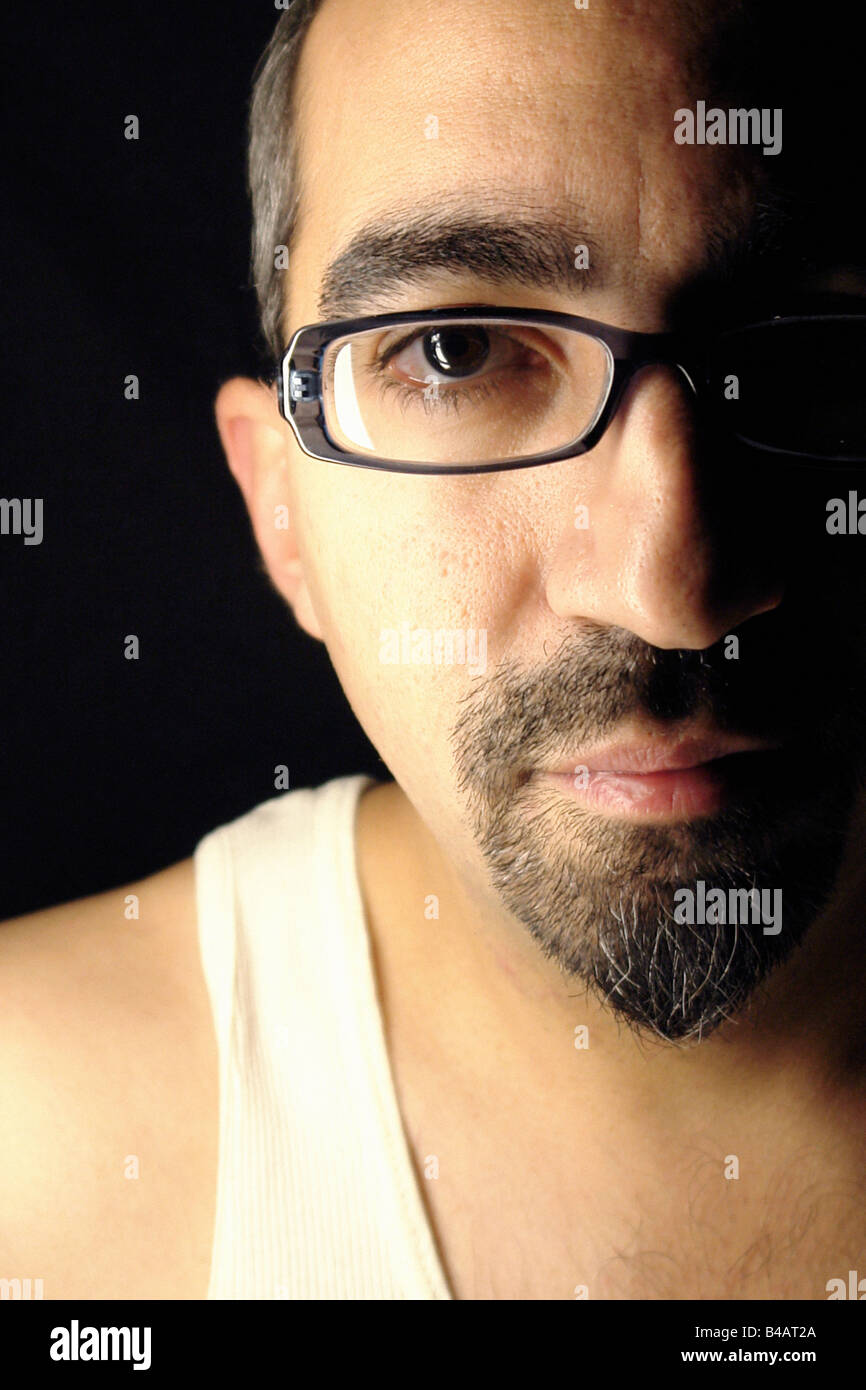 Side lit Portrait of a man of Hispanic Ethnicity He is wearing eyeglasses and a white tank top singlet Half face copy space Stock Photo