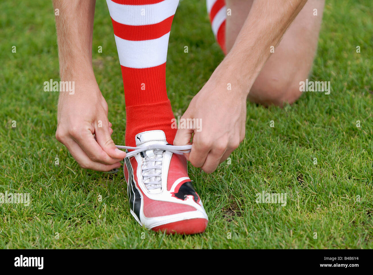 Soccerplayer laces up his red and white Puma soccershoes Stock Photo