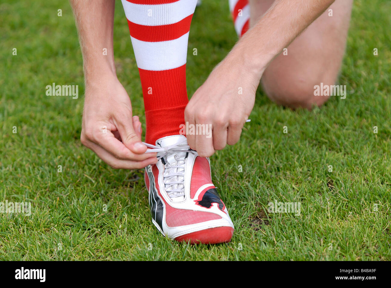 Soccerplayer laces up his red and white Puma soccershoes Stock Photo