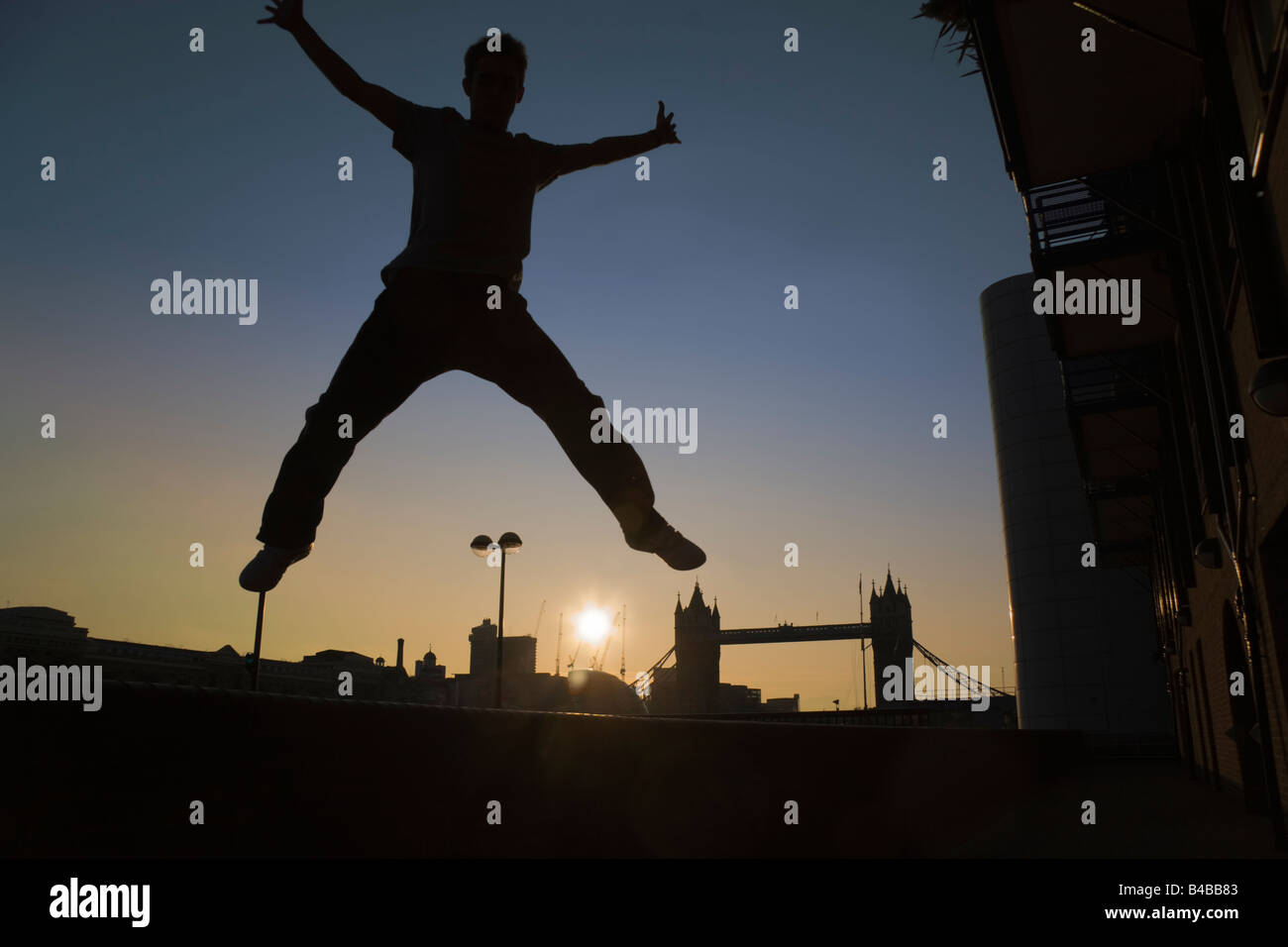 Silhouette of a young man jumping with his arms and legs outstretched near Tower Bridge in London Stock Photo