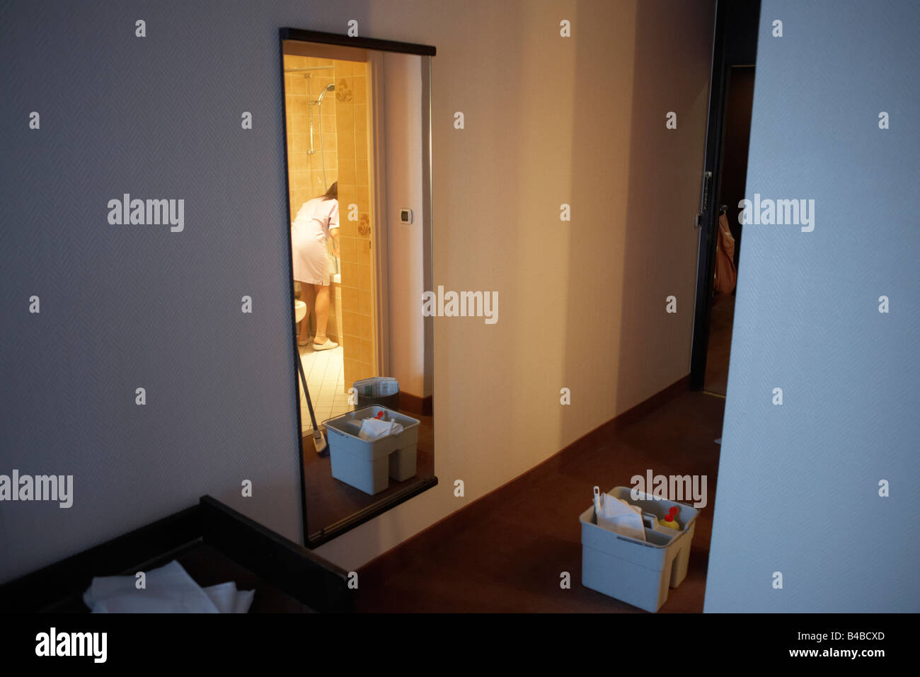 Using a mop and bucket  a chamber maid bends over in a bathroom to service a Paris hotel room. Stock Photo