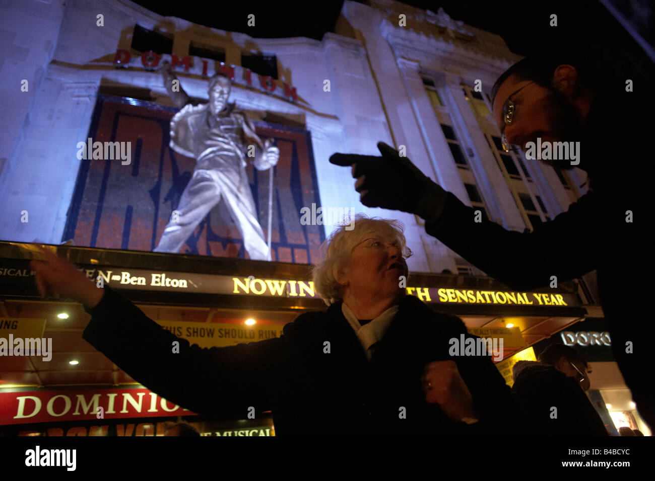 Lady visitor to London's Theatreland gets directions from a passer-by beneath a Freddy Mercury outside the Dominion Theatre Stock Photo