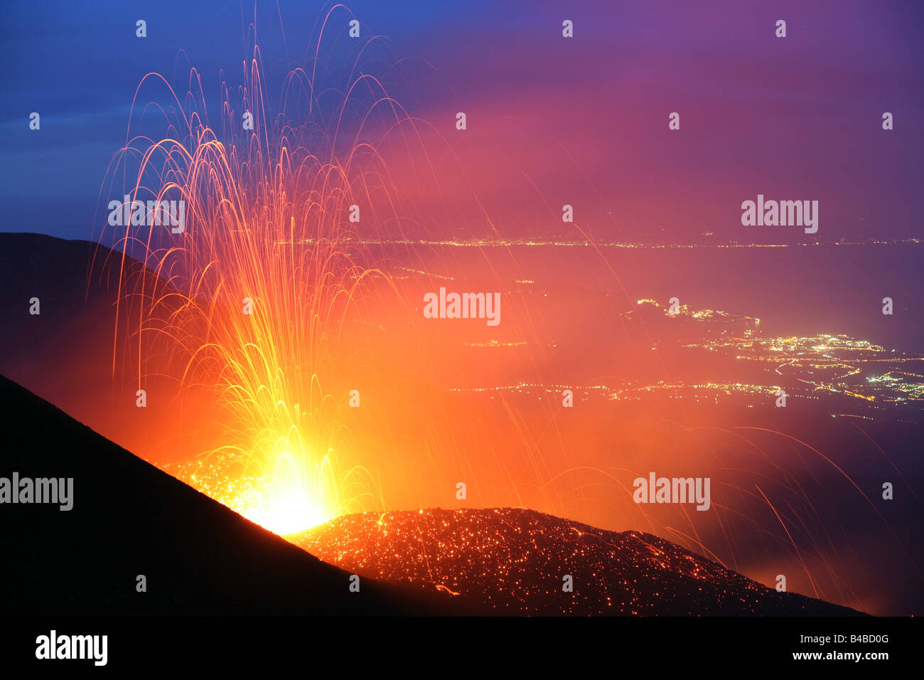 Volcanic eruption from Mt. Etna volcano, Sicily, in the evening with lights of Taormina and Giarre in the background Stock Photo
