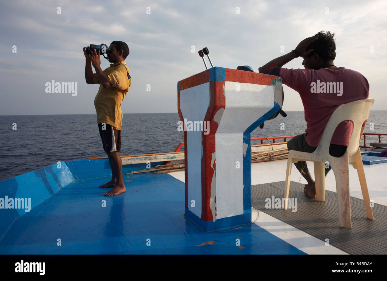 Using binoculars to sight yellowfin tuna on the upper deck aboard a traditional dhoni fishing boat on the Indian Ocean, Maldives Stock Photo