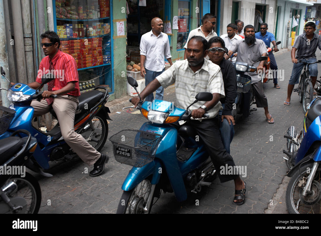 Motorcycles, mopeds and their helmetless riders crowd a narrow urban ...